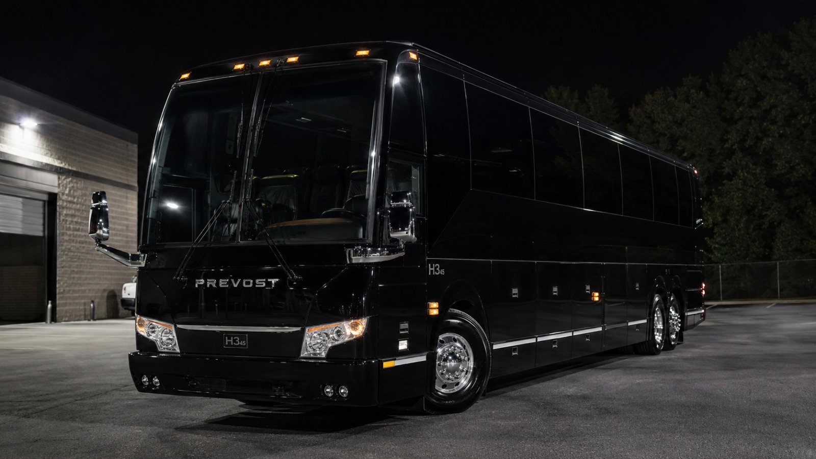 A black motorcoach parked outside a depot at night