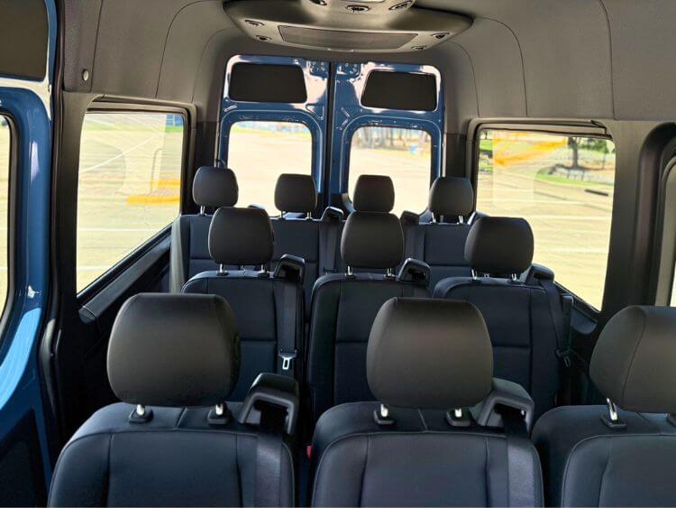 Rows of black leather passenger seats inside the Mercedes Sprinter, looking toward the rear